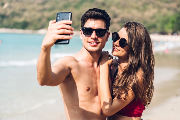 Romantic lovers young couple relaxing together on the tropical beach.Man and woman taking selfie with smartphone and enjoy life.Summer vacations