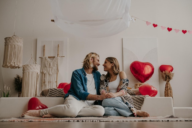 Romantic loving couple holding hands and leaning on bed with red heart shape balloons on background