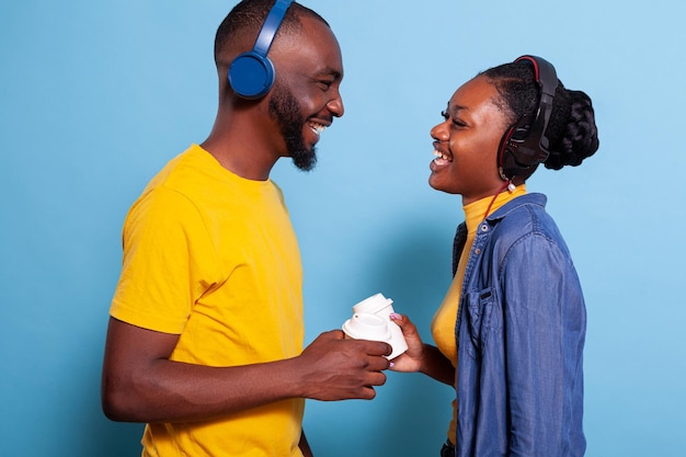 Romantic people having fun with radio music on headphones, listening to love song over blue background. Cheerful man and woman wearing headset to enjoy audio sound on mp3 playlist.