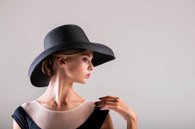 Romantic portrait of beautiful young girl on a light background in an elegant hat