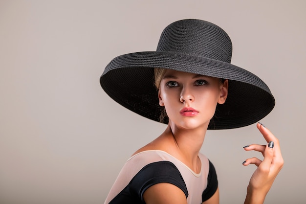 Romantic portrait of a beautiful young girl on a light background in an elegant hat