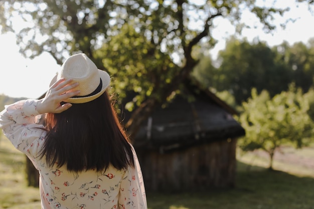 Romantic portrait of a young woman in straw hat and beautiful dress in the countryside in summer