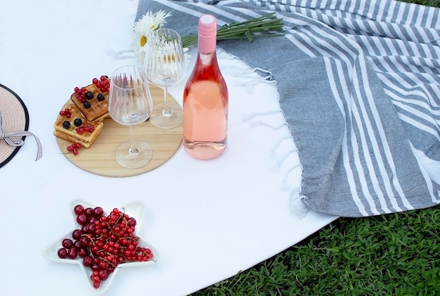 Romantic summer picnic in park on the grass Champagne and two glasses on white plaid Concept of food and drink