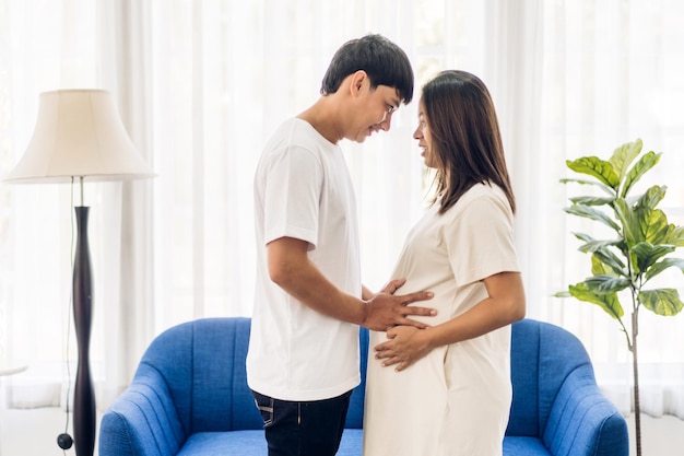 Romantic sweet asian couple husband hugging and smiling beauty asian pregnant wifeMan expecting with woman pregnancy hold to baby in belly at home