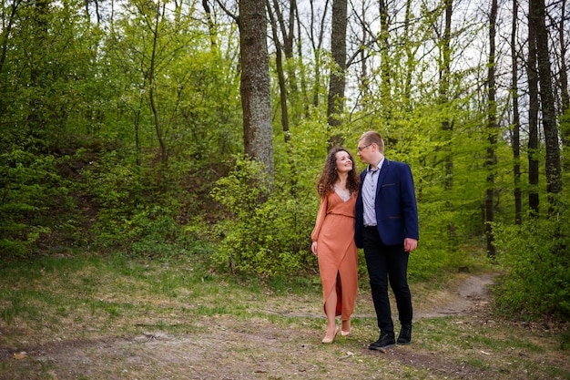 Romantic walk of a young couple in a green forest, warm spring weather. Guy and girl hugging in nature