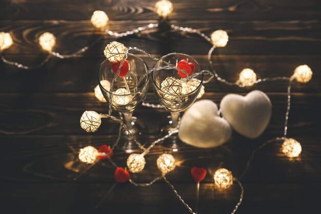 Romantic wine glasses with hearts for Saint Valentine's day Romantic date and dinner Cosy lights Wooden background Holiday postcard Love concept