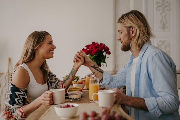 Romantic young couple holding hands while enjoying healthy breakfast at boho style home