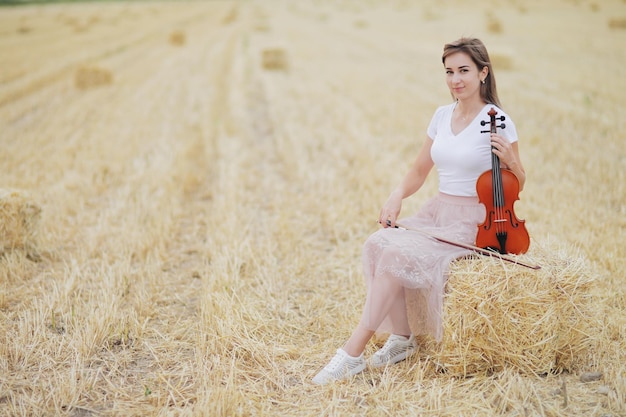 Romantic young woman with flowing hair holding a violin in her hand in a field