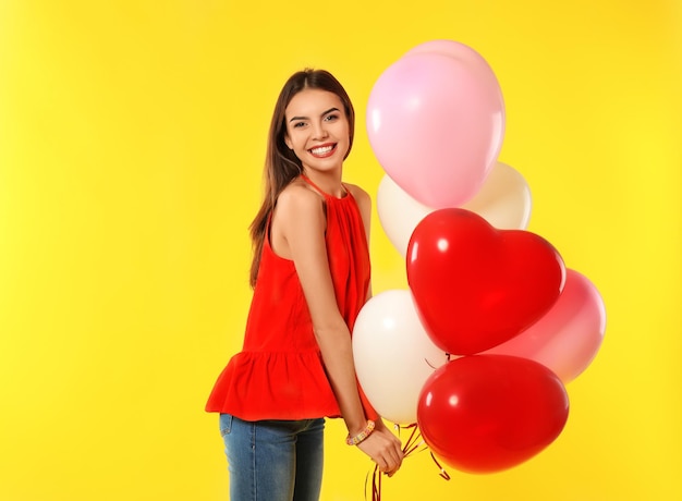 Romantic young woman with heartshaped balloons for Valentine's Day on color background