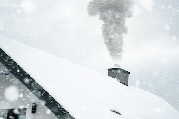 The roof of the family house in winter Winter landscape with falling snow and the smoke from a chimney heating a home during the chilly season