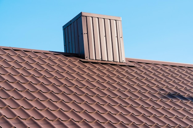 The roof of a house with modern metal tiles and a chimney against the background of a blue sky