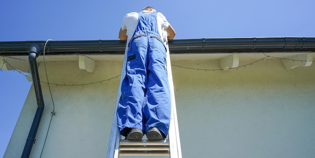 Roofer repairing the house roof Roofer at work Roofer standing on the metal ladder