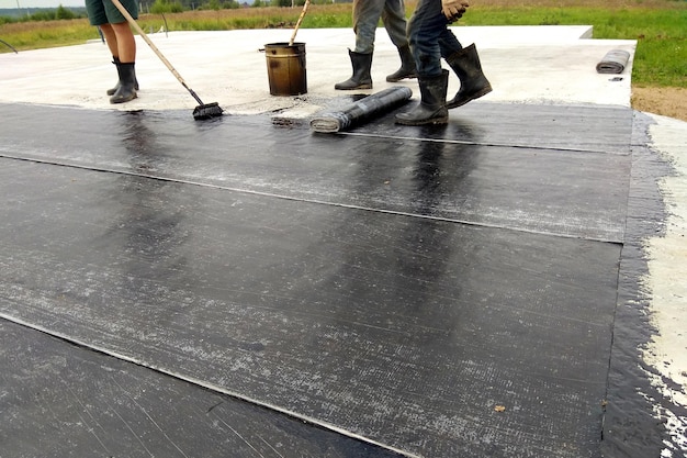 Roofer worker painting bitumen praimer at concrete surface by the roller brush Waterproofing