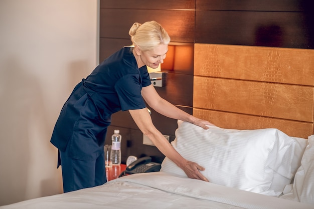 Room service. Blonde pretty woman in uniform making bed in a hotel room