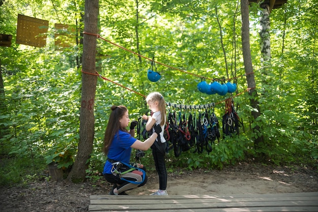 Rope adventure a woman instructor puts on the insurance pendants on the waist of a little girl