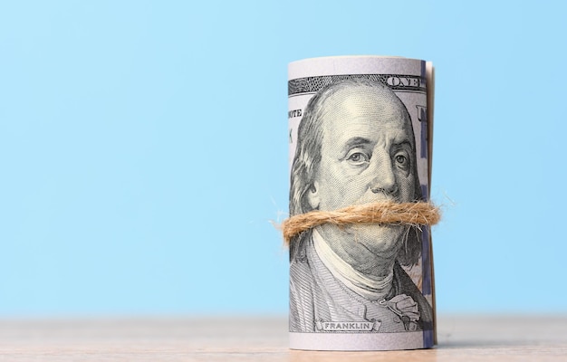 Rope tied roll of one hundred dollar bills on a blue background