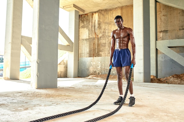 Rope workout Sport man doing battle ropes exercise outdoor Black male athlete exercising doing functional fitness training with heavy rope