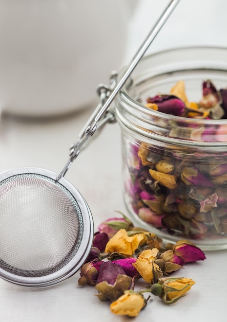 Rose buds mix tea in glass jar with vintage strainer infuser on white background