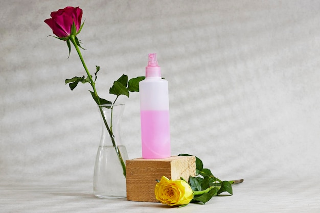 Rose essential oil or water on wooden cube and pink and yellow roses flowers on gray background win