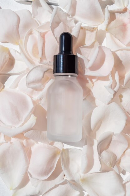 Rose flower petals and with aromatherapy essential oil glass bottle glass bottles with a pipette with serum or cosmetic oil lies on rose petals for face and body