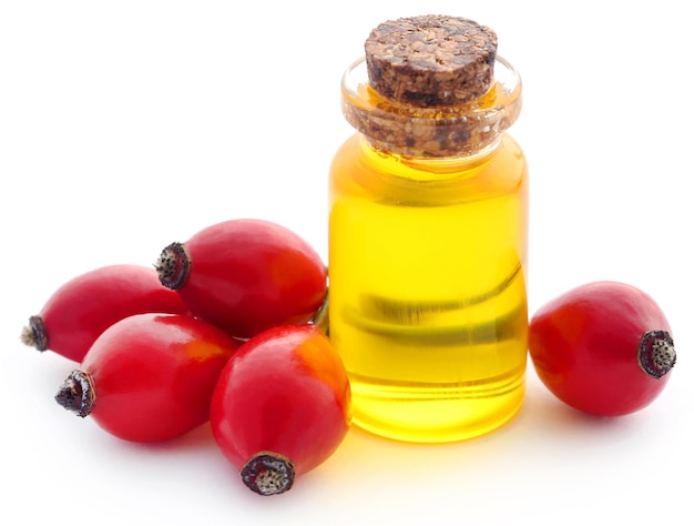 Rose hips with essential oil in a bottle over white background