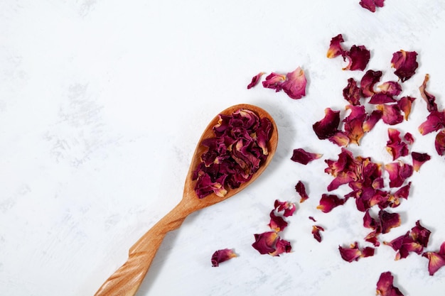 Rose petals in wooden spoon top view Dried Purple Rose petals on light grey textured table