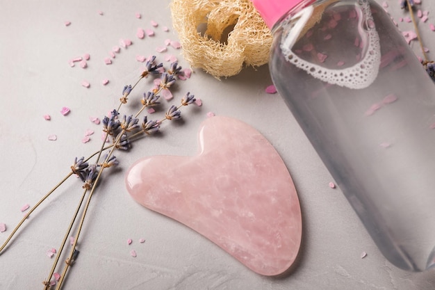 Rose quartz gua sha tool dried lavender flowers and cosmetic product on grey table closeup