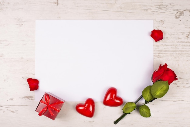 Rose two decorative hearts and a gift box lie on a table with a sheet of paper for congratulations