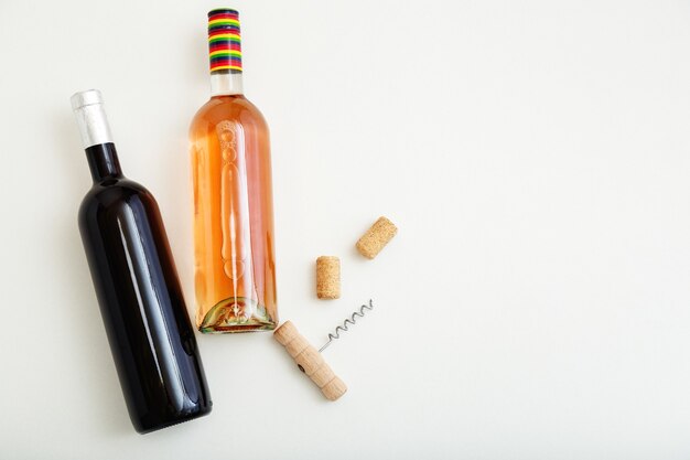 Rose wine bottle and red wine bottle corkscrew and cork. Minimalistic wine composition top view on white background. Two bottles of Wine brand mockup. Flat lay with copy space.