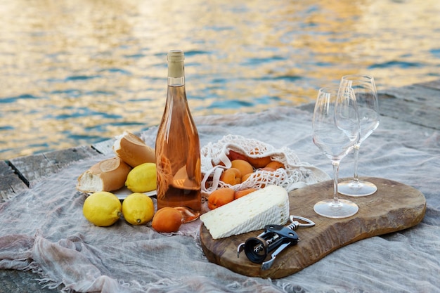 Rose wine fruits and snacks on the wooden pier during picturesque picnic on the wooden dock