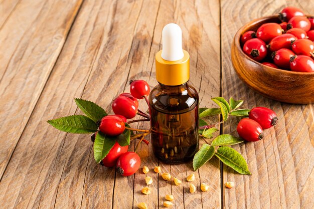 Rosehip oil in a glass cosmetic bottle on a wooden background and a bowl of ripe fruits the concept of combating skin aging prevention of wrinkles