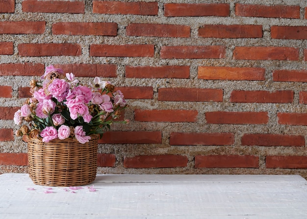 Roses in basket on wooden table against brick wall