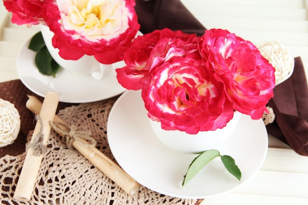 Roses in cups on napkins on wooden background