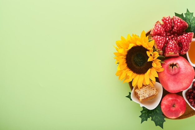 Rosh Hashanah Ripe pomegranate apple honey and sunflower yellow flowers on green background composition with symbols jewish Rosh Hashanah holiday attributes Top view with copy space