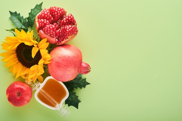 Rosh Hashanah Ripe pomegranate apple honey and sunflower yellow flowers on green background composition with symbols jewish Rosh Hashanah holiday attributes Top view with copy space