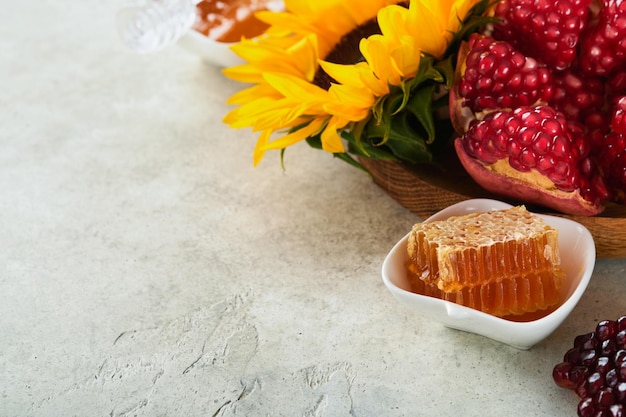 Rosh Hashanah Ripe pomegranate apple honey and sunflower yellow flowers on rustic grey background Composition with symbols autumn jewish Rosh Hashanah holiday attributes Top view with copy space