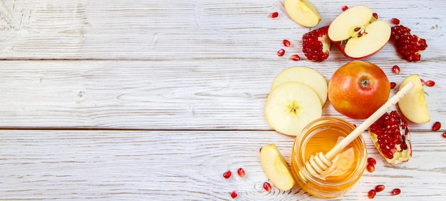 Rosh Hashanakh Jewish religious holiday Banner format Apples pomegranates and honey on white wooden background Traditional symbols