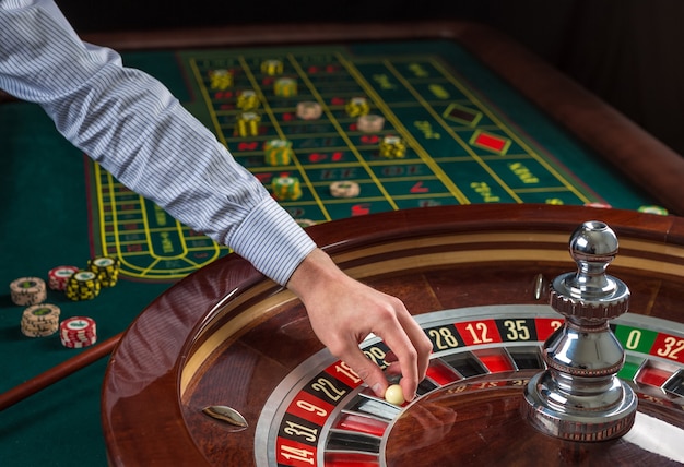 Roulette wheel and croupier hand with white ball in casino close up details