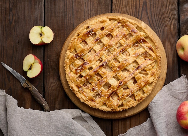 Round baked pie with apple filling on a wooden board brown table