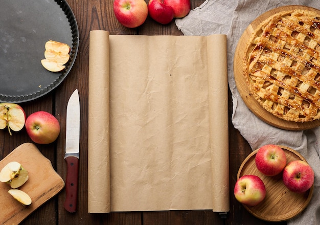 Round baked pie with apple filling on a wooden board and ingredients brown table