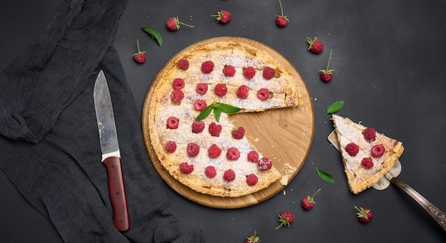 Round baked pie with apples and sprinkled with powdered sugar on a black table