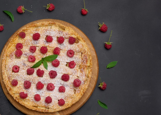 Round baked pie with apples and sprinkled with powdered sugar on a black table