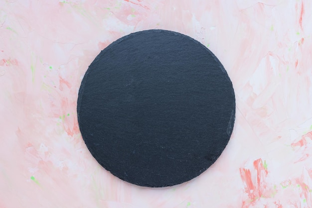 Round black slate plate on pink spring background Kitchen stone tray for serving food Black granite circle board Empty space for menu or recipe Top view copy space mockup