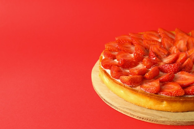 Round board with strawberry tart on red background.