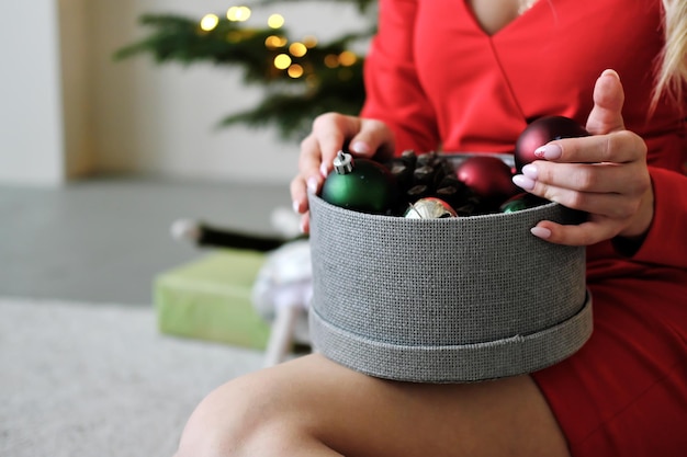 Round box with Christmas toys in female hands against the background of Christmas lights