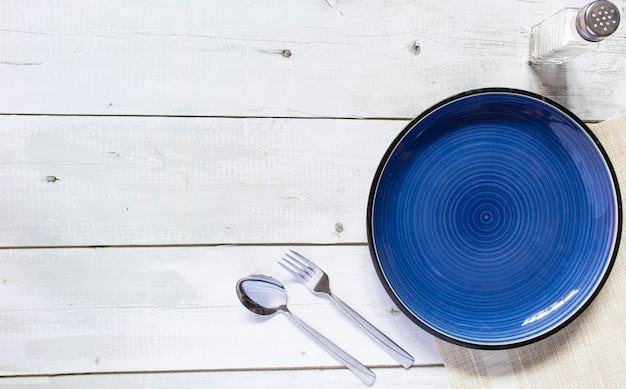 Photo round ceramic empty plate dark blue placed on the table concrete black and white texture background have salt placed bottle and spoon fork, top view, mockup for a restaurant dish.