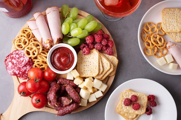 A round charcuterie board with sausage, cheese, crackers and fruit, plates with appetizer, close-up.