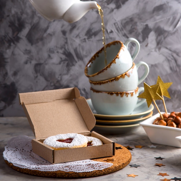 Round cookies with jam in the shape of a heart in a gift box among Christmas decorations and stars on a gray background