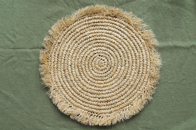 Round crochet jute coaster on wrinkled green linen fabric background