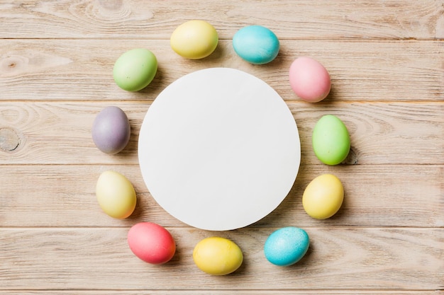 Round frame multicolored Easter eggs with white blank paper on a brown background closeup space for text blank for design selective focus tinted image